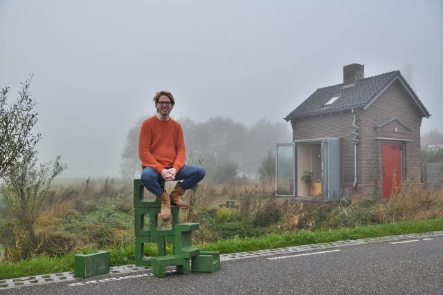 Ronald van der Zwaag zit op groene gasbetonblokken voor een heel klein huisje met open raam